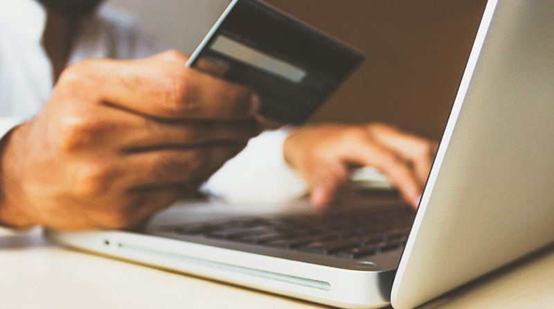 Man on laptop, looking at credit card representing enumeration attack