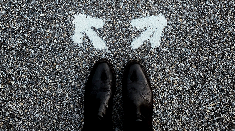 A man with dress shoes standing on the pavement with two arrows on the ground pointing in different directions representing bot prevention