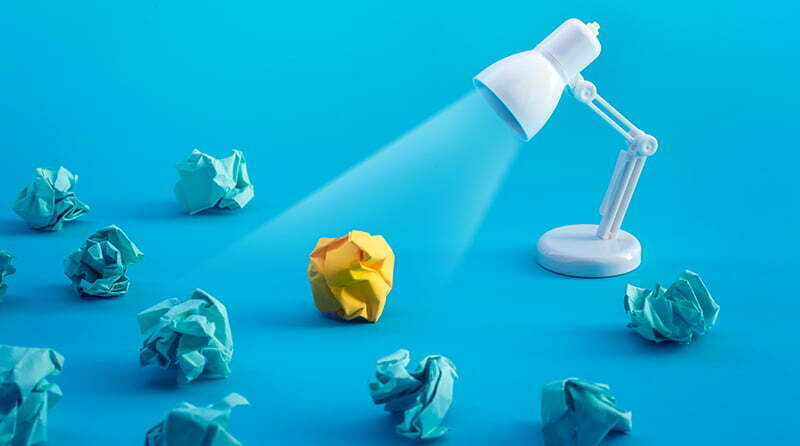 A desk lamp with several blue crumbled balls of paper shining it's light on a yellow balled up paper representing api visibility security