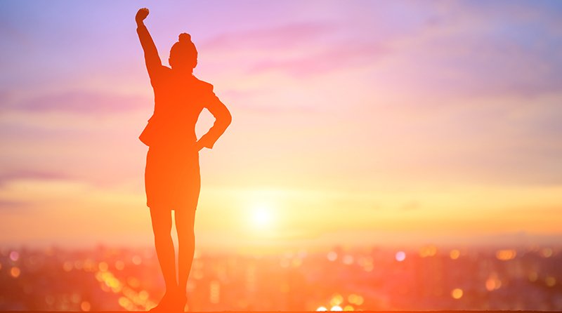 Woman standing overlooking a city with her arm raised representing recognizing women