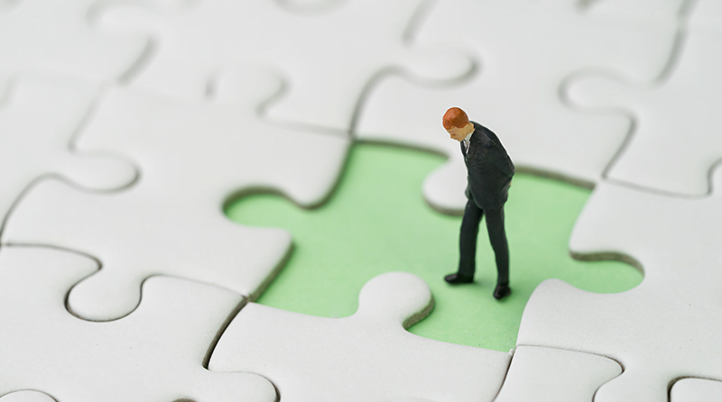 A puzzle with a missing piece and a toy business man standing in the missing piece looking down representing API Security